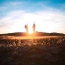 Two people jumping in the reflective sunlight in a field with the mountains behind them.