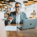 guy with glasses and a MacBook holding a pen and smiling
