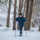 A man cross country skiing with a blue and black coat on and a black toque.