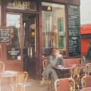 A middle aged women sitting at a French cafe drinking coffee and people watching