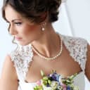 A wedding portrait of a brunette bride wearing pearls and holding a blue and pink bouquet of flowers.