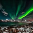A dramatic photo of the Northern Lights in a beautiful landscape with water and mountains